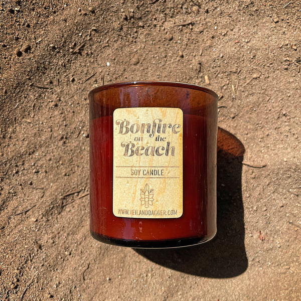 bonfire on the beach soy wax candle with wood wick in amber glass tumbler jar on sandy beach