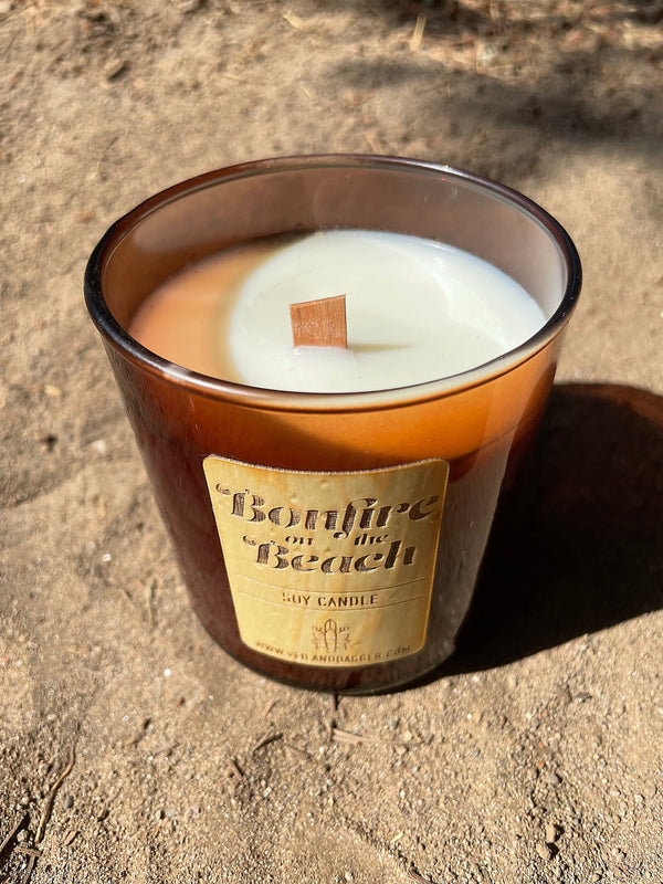 bonfire on the beach soy wax candle with wood wick in amber glass tumbler jar on sandy beach
