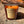 Load image into Gallery viewer, Bonfire on the beach scented soy candle by Veil and Dagger Fine Home Goods sitting on sand by driftwood on the beach