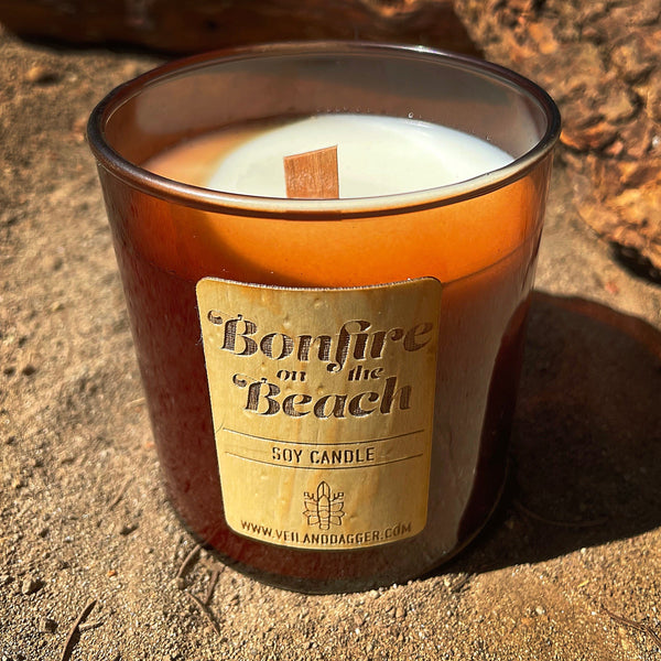 bonfire on the beach soy wax candle with wood wick in amber glass tumbler jar on sandy beach