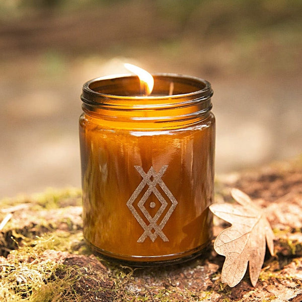 Woodsman 1 pine cedarwood leather scented soy candle laser etched nordic design amber jar sitting on mossy log with oak leaf