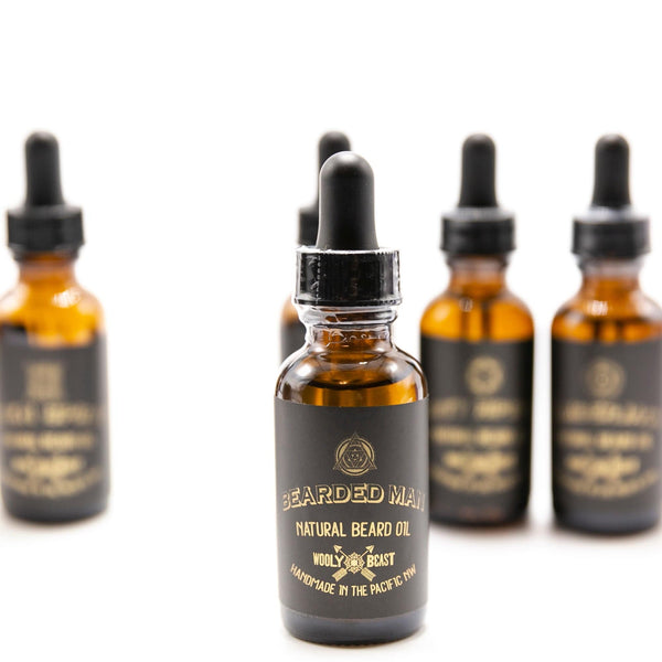 Bearded man natural beard oil in an amber bottle with 1oz dropper with other beard oils on white background black and gold label has sacred geometry design and says Bearded man natural beard oil wooly beast handmade in the pacific nw