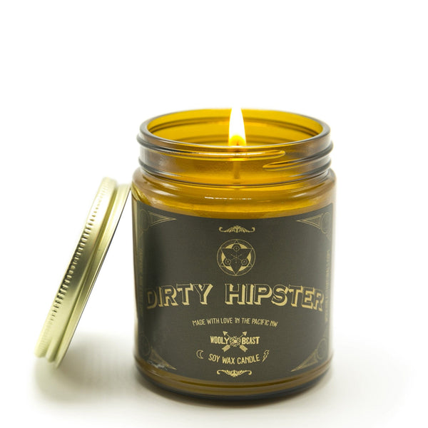 Dirty Hipster Soy Candle wick burning with gold lid leaning against the side against white background. Black and gold label has sacred geometry design and says Soy Wax Candle made with love in the pacific nw