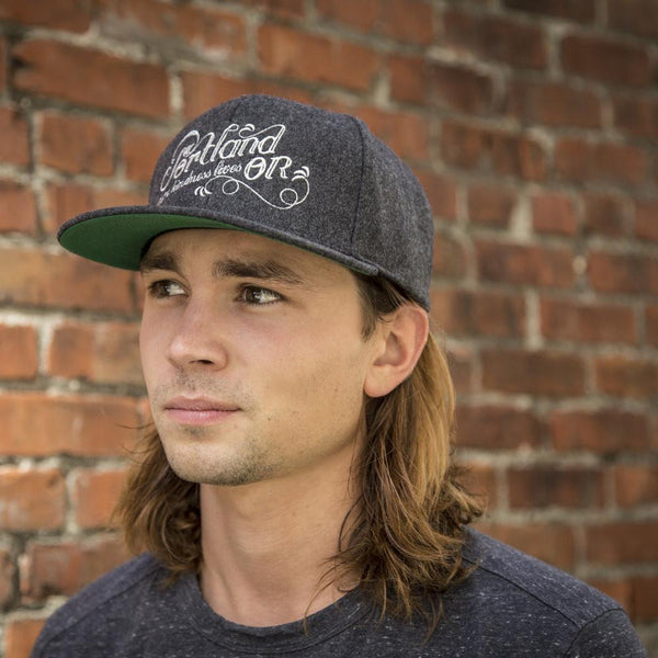 Portland Oregon Hat in grey wool on male model with shoulder length hair against vintage brick background