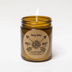 cotton wick soy candle burning in glass amber threaded apothecary jar on white background. Circle kraft paper labels reads Sleep Baby Wooly Beast crossed arrows logo soy wax candle handmade in portland oregon