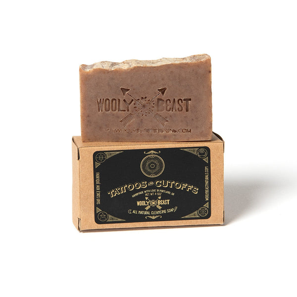 Tattoos and Cutoffs natural bar soap on white background, bar soap is on top of kraft paper box packaging on white background, black and gold label has sacred geometry design and reads Tattoos and Cutoffs handmade with love in portland, or wooly beast all natural cleansing soap