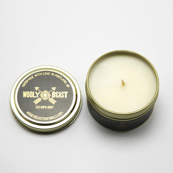 overhead pov shot of soy wax candle in gold metal tin. Gold lid sits to left side on white background. Lid reads Handmade with love in portland, oregon. Wooly Beast crossed arrows logo, eco home and body, woolybeastnaturals.com